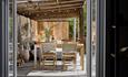 View through open doors into a cosy outdoor dining area with wooden table, chairs, plants, and soft lighting.