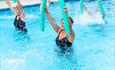 four people in a swimming pool with green pool noodles