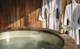 A steaming hot tub with two white robes and two glasses of champagne.