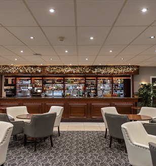 Elegant bar interior decorated for the holidays, featuring a wooden counter adorned with garlands, cozy seating, a festive tree, and a warm ambiance.